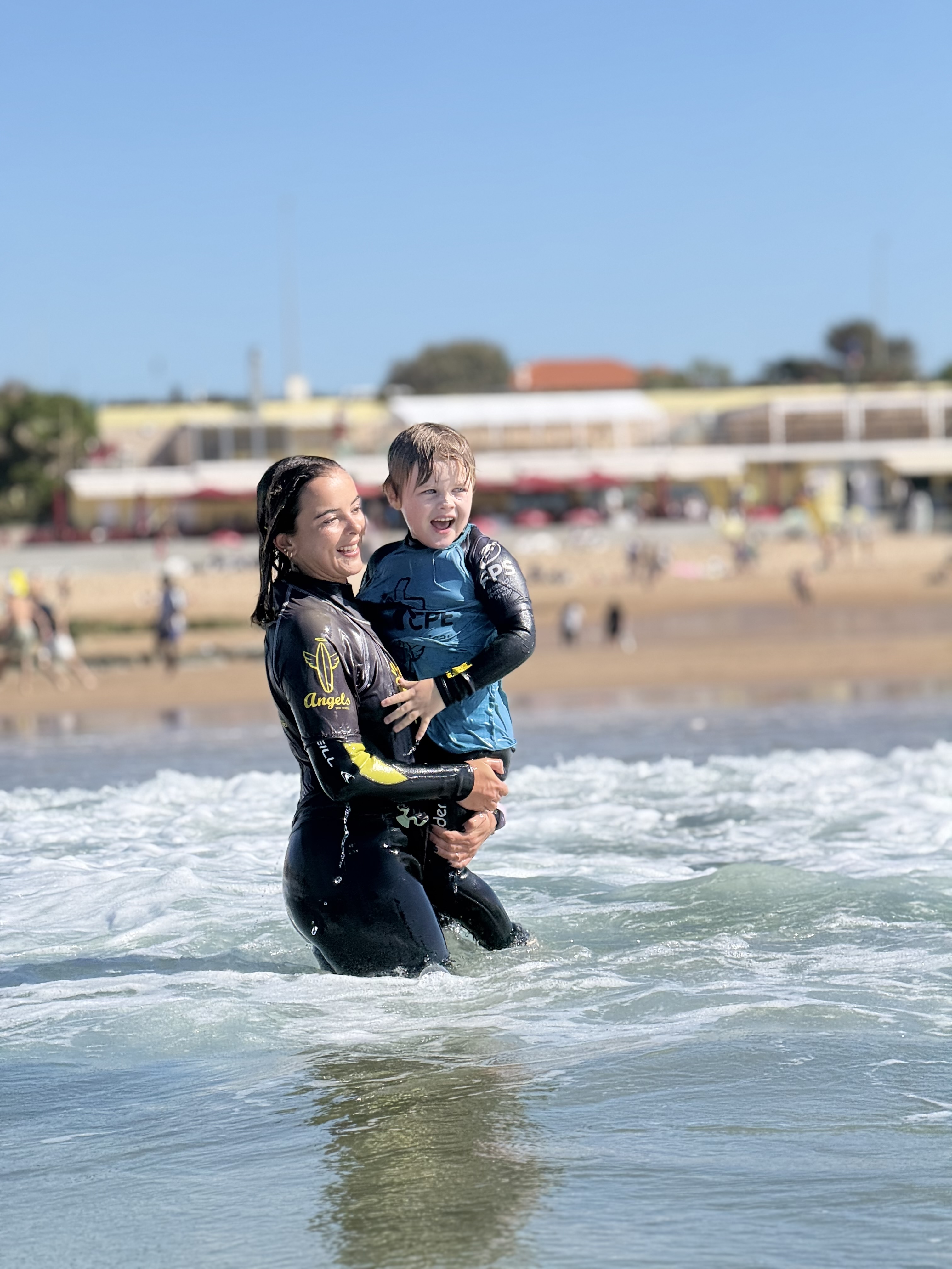 Instrutora Kids Care com criança no mar, criança de braços abertos em vitória
